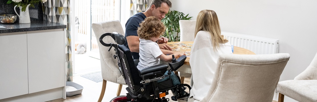Boy in wheelchair playing a game with his parents.