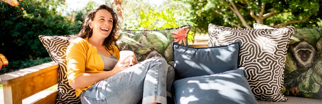 woman sits on a couch with a drink smiling.